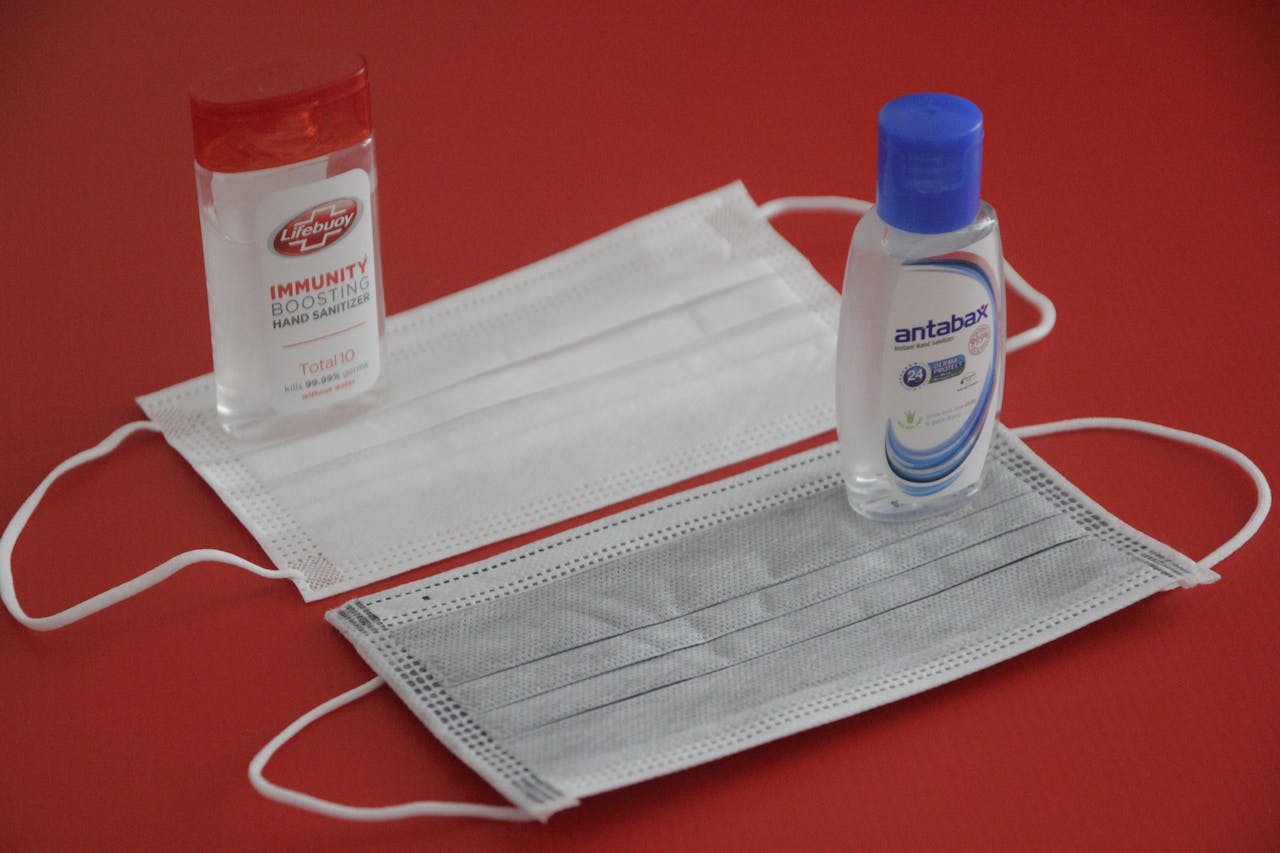 hero-img Close-up of face masks and sanitizers on a red surface, emphasizing hygiene.